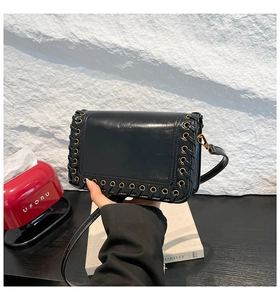 Detailed view of woven black leather edge with gold eyelets on a square crossbody bag