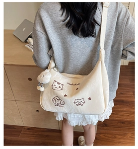 Detail of cream tote bag with cat embroidery and plush charm in a cozy indoor setting