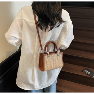 Detail of a brown leather and straw woven crossbody bag with a round handle and metal clips