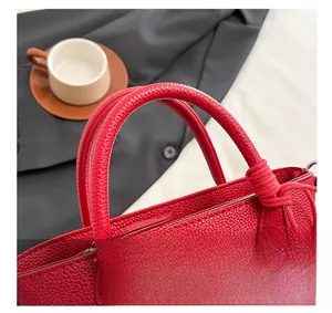 Gros plan du sac en cuir rouge à grain litchi avec poignée nouée et détails argentés