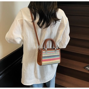 Detailed view of the multi-colored woven handbag with brown leather straps worn by a model
