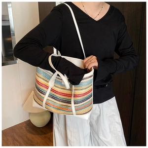 Detailed view of model carrying a large colorful striped straw tote bag with white leather straps