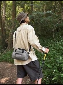 Outdoor scene of a grey nylon crossbody bag for hiking with logo and waterproof fabric detail