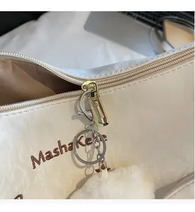 Detail of metal zipper and white plush ball pendant on a textured beige tote bag