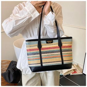 Close-up of a colorful woven straw tote bag with black leather straps and gold metal plaque