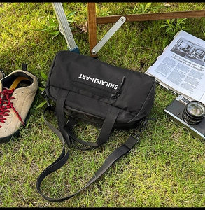 Outdoor close-up of a black nylon bowling sports bag on grass with travel accessories