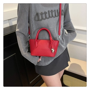Détail du sac seau rouge avec texture litchi et pendentif cœur porté par un modèle