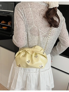 Pale yellow pleated cloud bucket bag featuring silver butterfly metal accents and chain strap