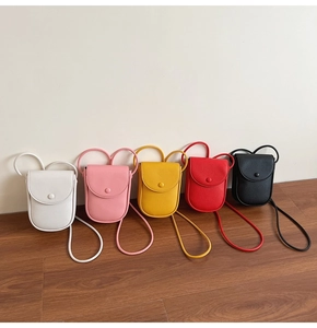 Cinq petits sacs bandoulière texturés de couleurs variées posés sur un sol en bois