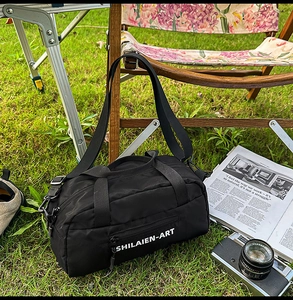 Close-up of black crossbody gym bag with SHILAIEN-ART logo on grass background