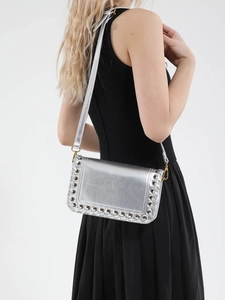 Chic silver metallic crossbody bag with eyelet details worn by model in black dress