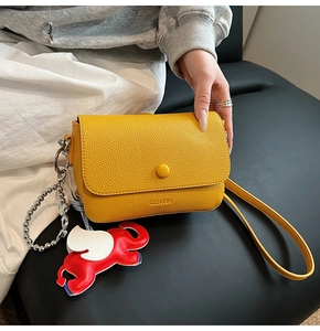 Detail of yellow lychee texture crossbody bag with cute red elephant charm and round buckle