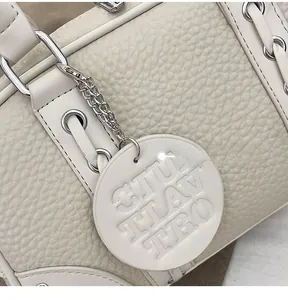 Detail of beige lychee grain leather handbag featuring silver chain and embossed charm