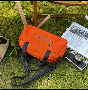 Close-up of orange nylon outdoor bag with blue handles on a wooden camping chair