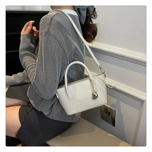 Détail d'un mini sac seau blanc à motif litchi avec pendentif cœur argenté sur modèle