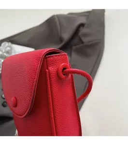 Détail du sac bandoulière en cuir grainé rouge montrant la texture et le rabat arrondi