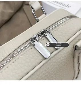 Detail of smooth metal dual zippers on cream-colored lychee textured leather handbag