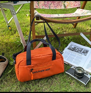 Detailed view of an orange crossbody bag on grass with a detachable strap and zipper pocket