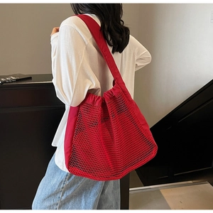 Detail of red hollow mesh tote bag worn by a model in a minimalist indoor setting