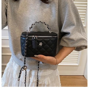 Détail du mini sac vanité noir matelassé avec anse chaîne et emblème de camélia