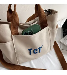 Détail du sac fourre-tout en toile beige avec poche avant et broderie TCT bleue