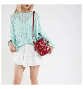 Nahaufnahme einer roten Nietentasche, kombiniert mit Mint-Strickpullover und weißem Rock