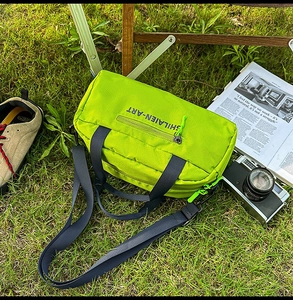 Outdoor nylon bowling bag in neon green on grass with camping accessories and strap
