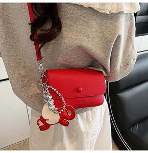 Detail view of red lychee grain leather crossbody bag with cute elephant charm