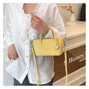 Détail du sac seau jaune avec texture litchi et pendentif coeur sur chemise blanche