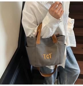 Détail du sac cabas en toile grise avec poignées marron et broderie jaune TCT élégante