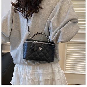 Détail du sac seau noir matelassé avec breloque camélia argentée et bandoulière chaîne
