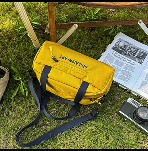 Outdoor yellow nylon sports bag with black handles on a scenic green lawn background