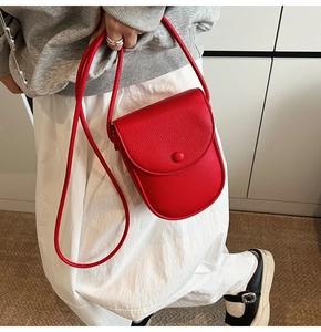 Détail du petit sac bandoulière rouge en cuir grainé avec rabat porté par un mannequin