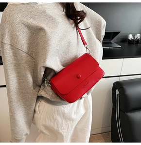 Close-up of red litchi texture crossbody bag with silver buckle on a stylish model