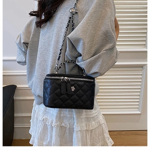 Détail d'un sac seau noir matelassé avec boucle fleurie argentée et bandoulière chaîne