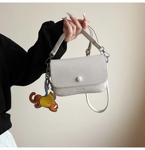 Detail of white lychee leather handbag with magnetic round clasp and cute elephant charm