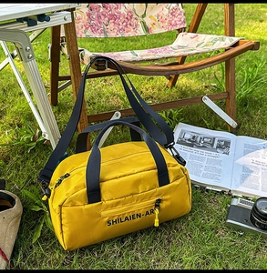 Outdoor close-up of yellow nylon crossbody bag with black handles on green grass