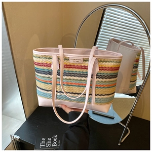 Close-up of colorful striped woven tote bag featuring a pink leather handle and logo detail