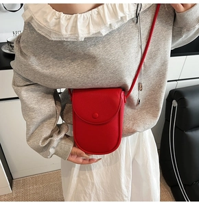 Détail d'un petit sac bandoulière rouge en cuir grainé porté par un mannequin