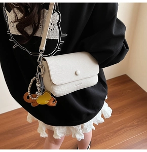 Detail of creamy white pebble grain shoulder bag with decorative charms and metal clasp