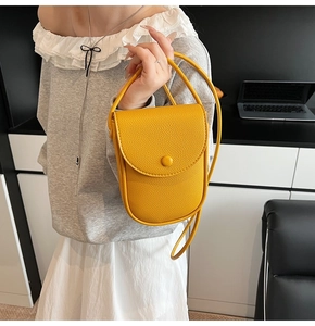 Détail du sac bandoulière en cuir jaune avec texture grainée et fermoir rond à pression