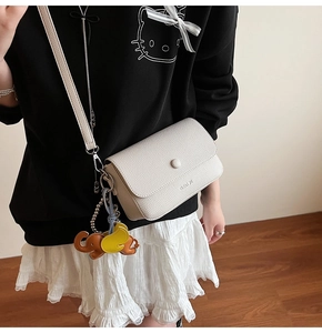 Detail view of off-white lychee grain leather crossbody bag with cute animal charms