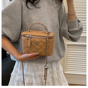 Gros plan du sac seau matelassé camel avec logo camélia et bandoulière chaîne
