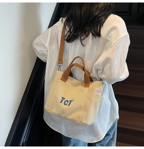 Gros plan du sac cabas en toile blanc cassé avec broderie TCT bleue et bandoulière brune