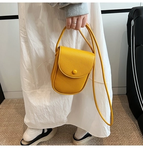Détail d'un mini sac bandoulière jaune avec texture grainée porté par un modèle