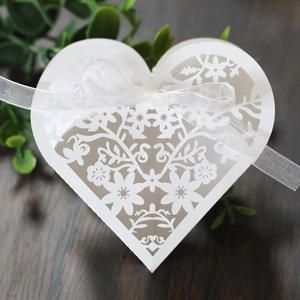 Close-up of white heart-shaped wedding favor box with laser-cut floral details and ribbon