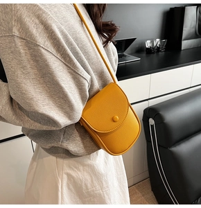Détail du sac à bandoulière en cuir grainé jaune vif porté par un mannequin en intérieur
