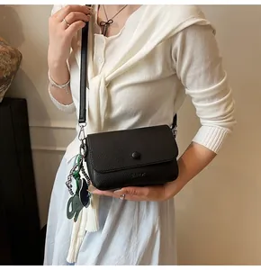 Detailed view of black litchi pattern leather crossbody bag with green elephant charm
