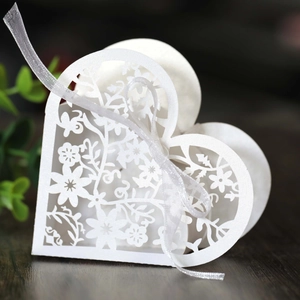 Detail of white laser-cut hollow heart candy box with floral patterns and silk ribbon