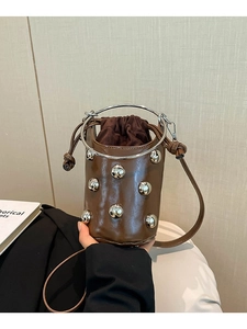 Braune Beuteltasche mit Nieten und Metallringgriff in einer Lifestyle-Szenerie